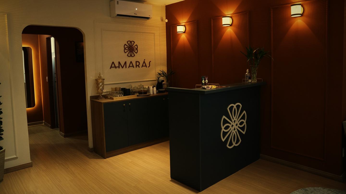 Recepção da Amarás Spa Vila São Francisco à noite: parede terracota com arandelas, letreiro Amarás e balcão com a mandala